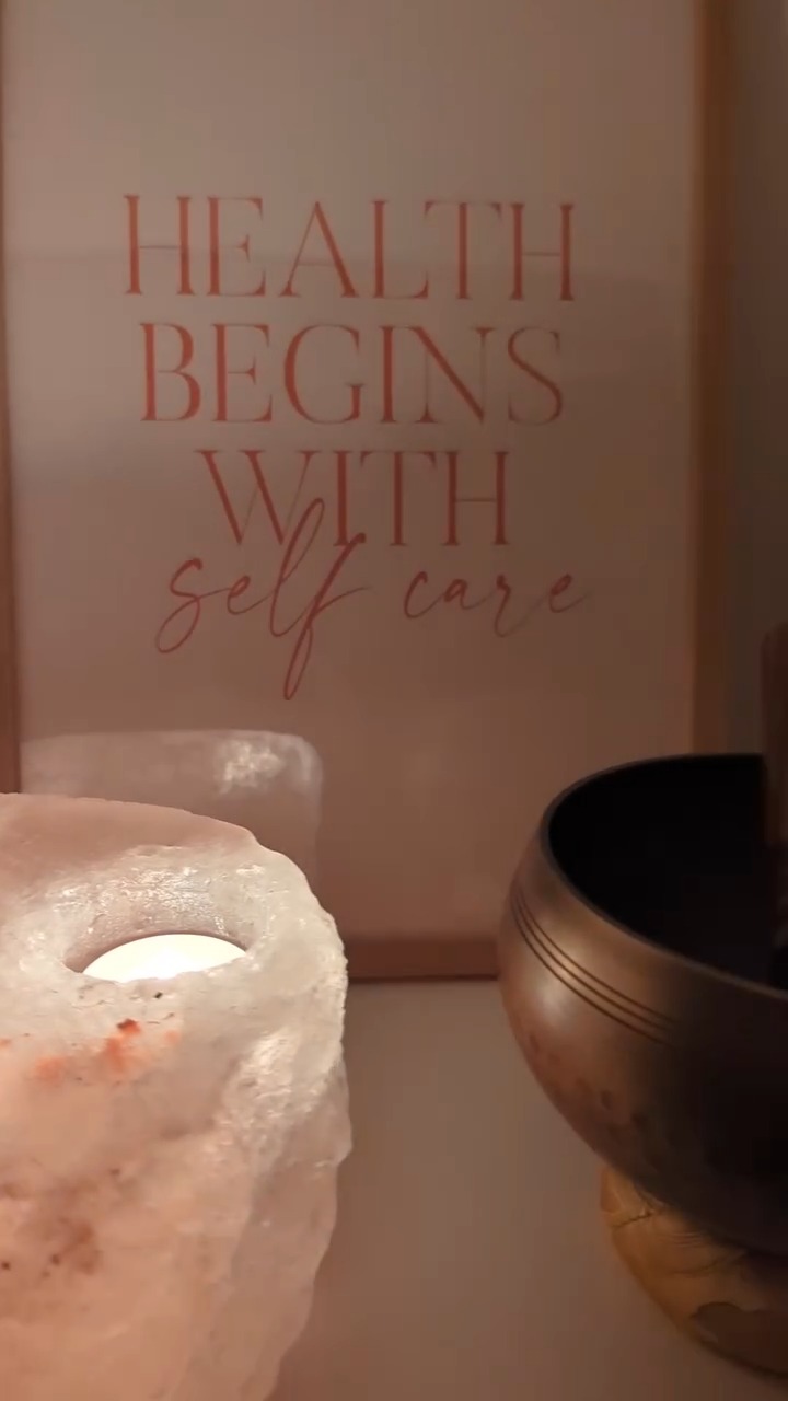 Roze zoutlamp met waxinelichtje, een klankschaal en een print met 'Health begins with self care'