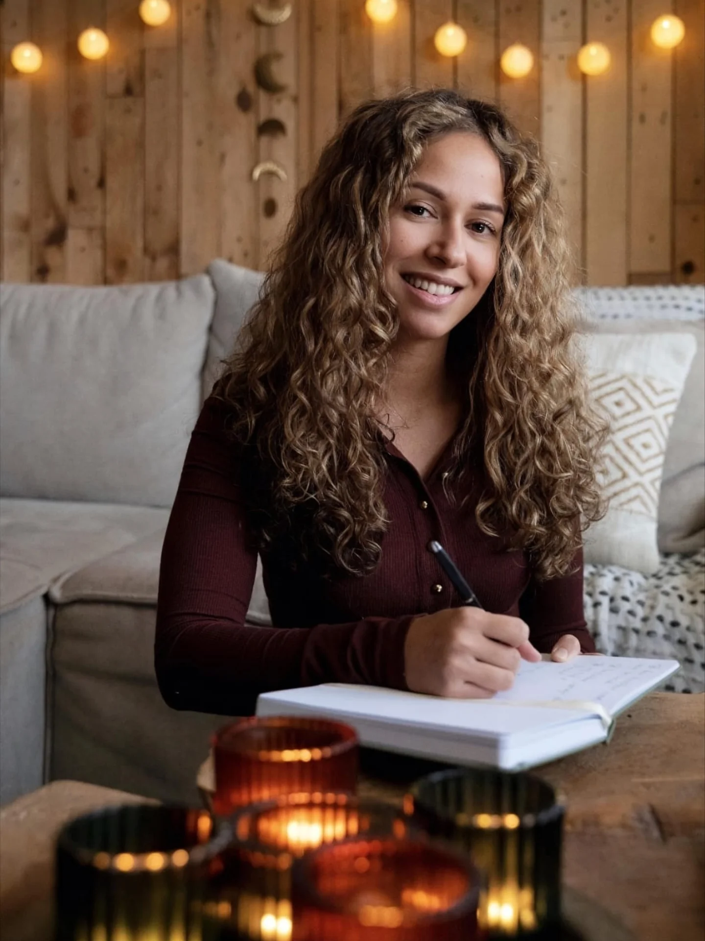 Siënna van IN BALANSI aan tafel met kaarsjes, achter haar een houten wand met lichtjes